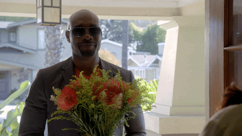 A man in a grey suit with sunglasses gives his partner a bouquet