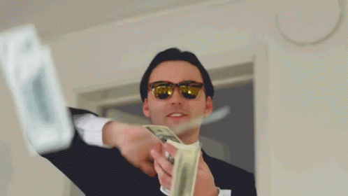 A man in a suit, wearing sunglasses making it rain some bills