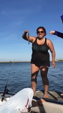 A woman is about to throw a fish back into the water but she falls into the water instead