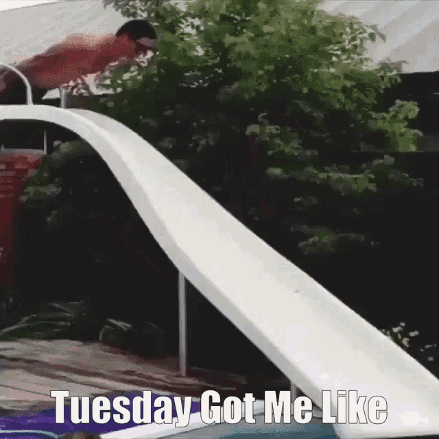 A man on the water slide tumbles off and lands on the edge of the pool